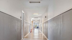 A long, narrow hallway with a smooth floor and plain walls, leading to a door at the end.