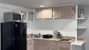 A modern kitchen with a black refrigerator, wooden cabinets, a microwave, and a coffee maker.