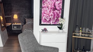 A modern bedroom with a grey sofa, a white dresser, and a large floral artwork on the wall.