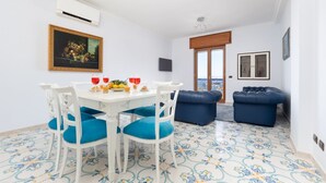 A dining area with a white table, blue chairs, and a painting on the wall. - Casa Cafarelli - Bright apt with Stunning view (Sorrento)