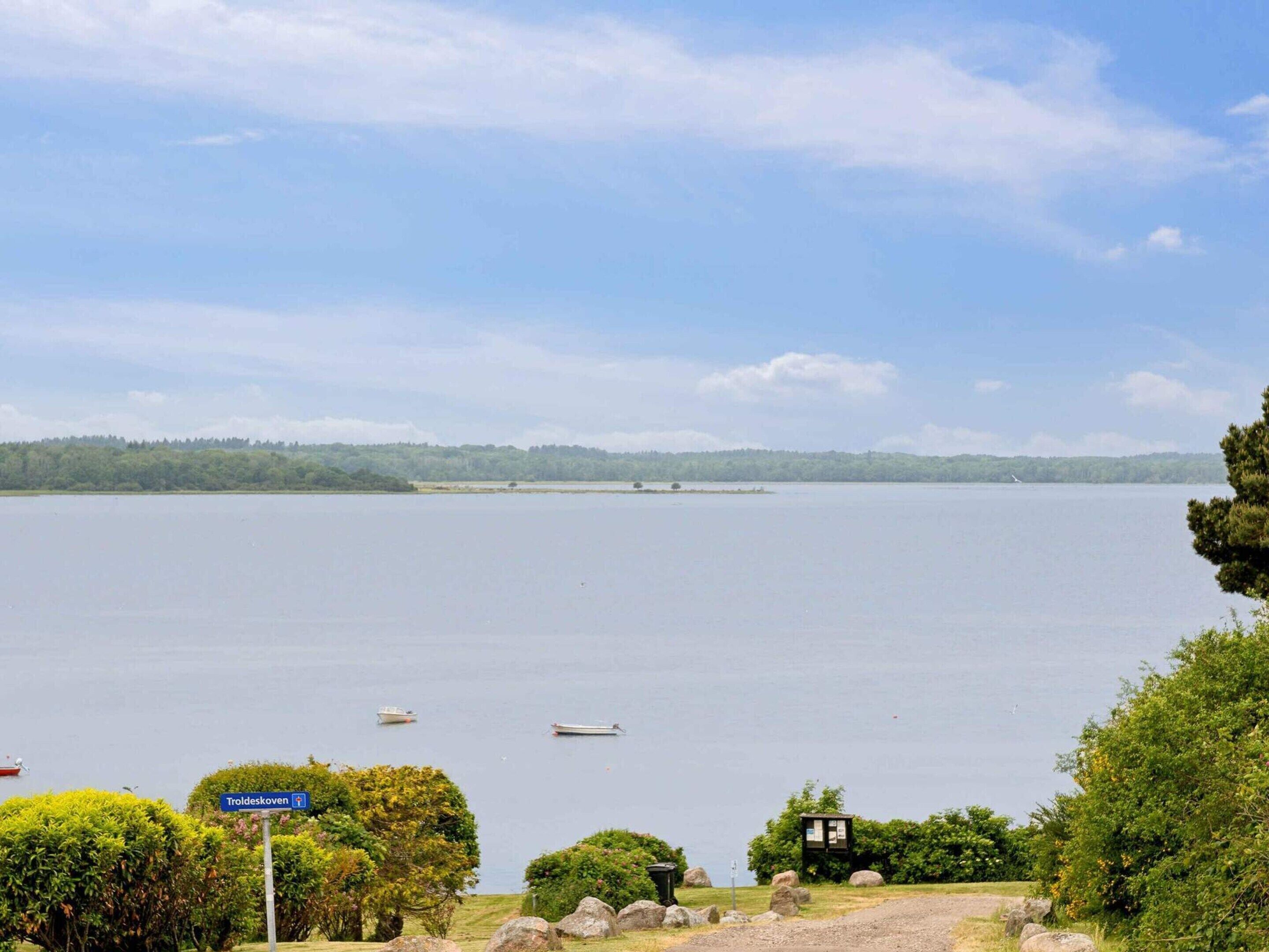 A lake with boats, a sign for 'Trolledskoven', and a small building, likely a shelter or information point.