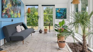 A modern living room with a grey sofa, two large abstract paintings, and a variety of potted plants. - 5 Star Holiday Home in Olsted (Olsted)