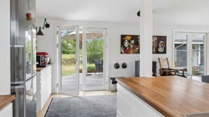 A modern kitchen with a large island, a built-in oven, and a dining area with a view of the garden. - 5 Star Holiday Home in Olsted (Olsted)