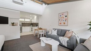 A modern living room with a grey sofa, white coffee table, and a dining area with a wooden table and chairs. - Hibiscus Villa - Pet Friendly, Spacious beachfront studio, private courtyard (Coffs Harbour)