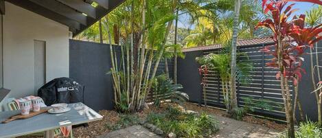A patio area with a table and chairs, surrounded by tropical plants and a fence.