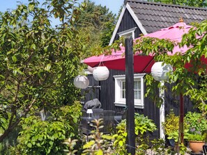 A black house with a red awning, surrounded by greenery and outdoor furniture. - 5 Star Holiday Home in Vejby (Vejby)