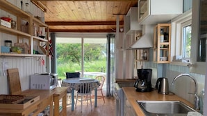 A compact kitchen with a wooden ceiling, a dining area with a table and chairs, and a large window offering a view of greenery. - 5 Star Holiday Home in Karrebaeksminde (Karrebæksminde)