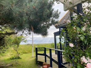 A wooden deck with a railing, a glass door, and a view of a grassy field and a tree. - 5 Star Holiday Home in Karrebaeksminde (Karrebæksminde)