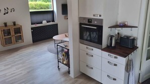 Eine moderne Küche mit Einbauofen, Kaffeemaschine und Toaster. Es gibt einen Holzkasten mit Glastüren und einen kleinen Tisch mit Stühlen.