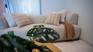 A cozy living room with a sofa, patterned cushions, a plant, and a wooden side table.