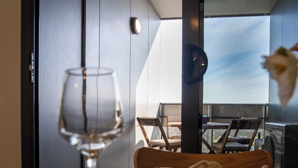 A dining table with a wine glass, plates, and cutlery, set against a modern interior with a view of the outdoors.