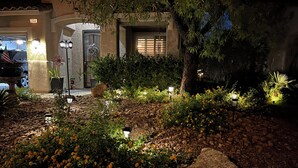 Un espacio exterior bien iluminado, con un sendero de piedra, una valla de madera y diversas plantas y flores.