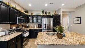 Una cocina moderna con gabinetes negros, electrodomésticos de acero inoxidable, encimera de granito y una isla central.