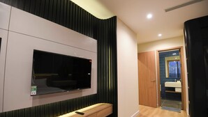 Un baño moderno con tocador de madera, televisor montado y zona de ducha visible.