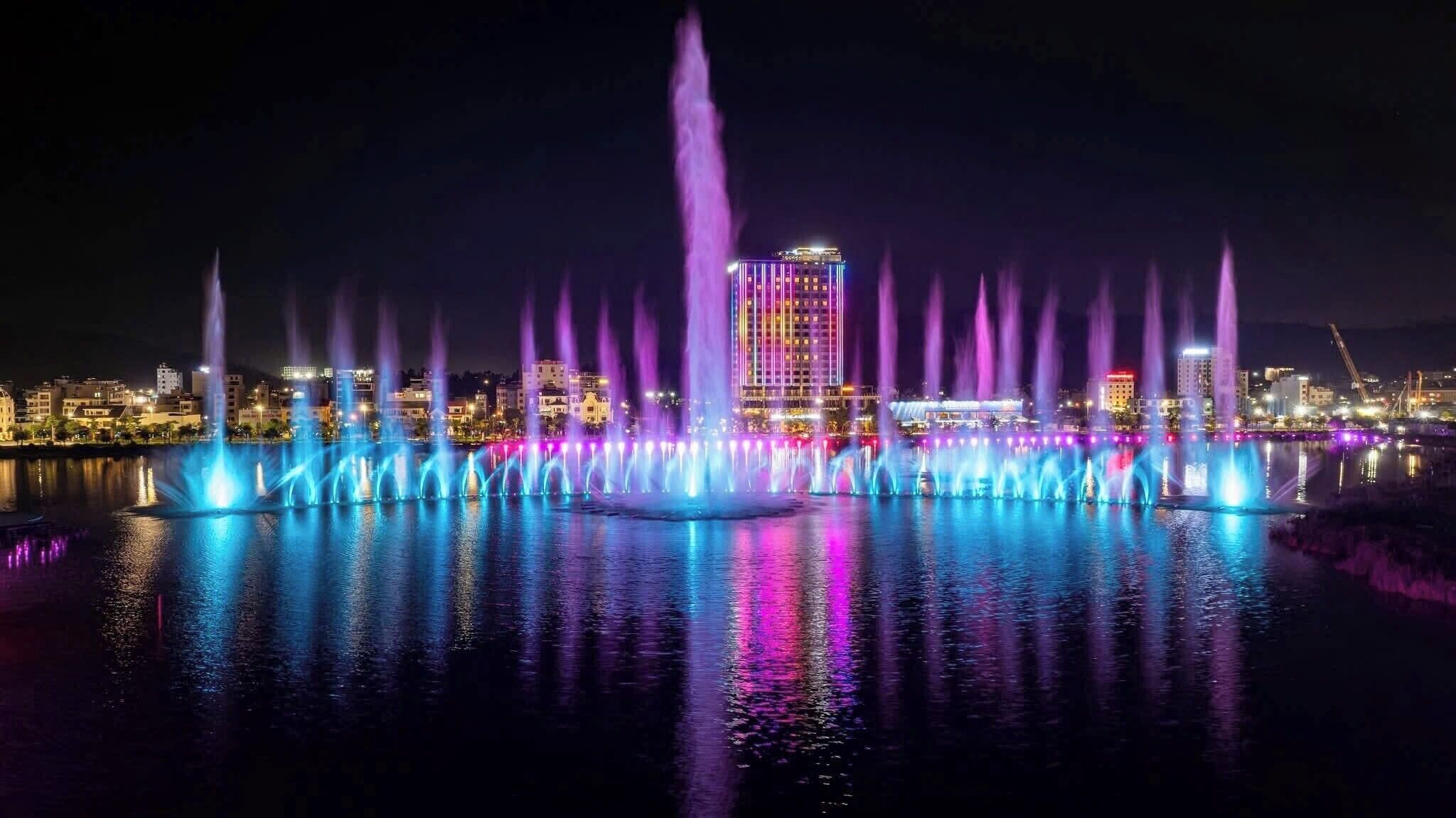 Une vue nocturne d’une ville, avec un bâtiment imposant au centre et une fontaine illuminée.