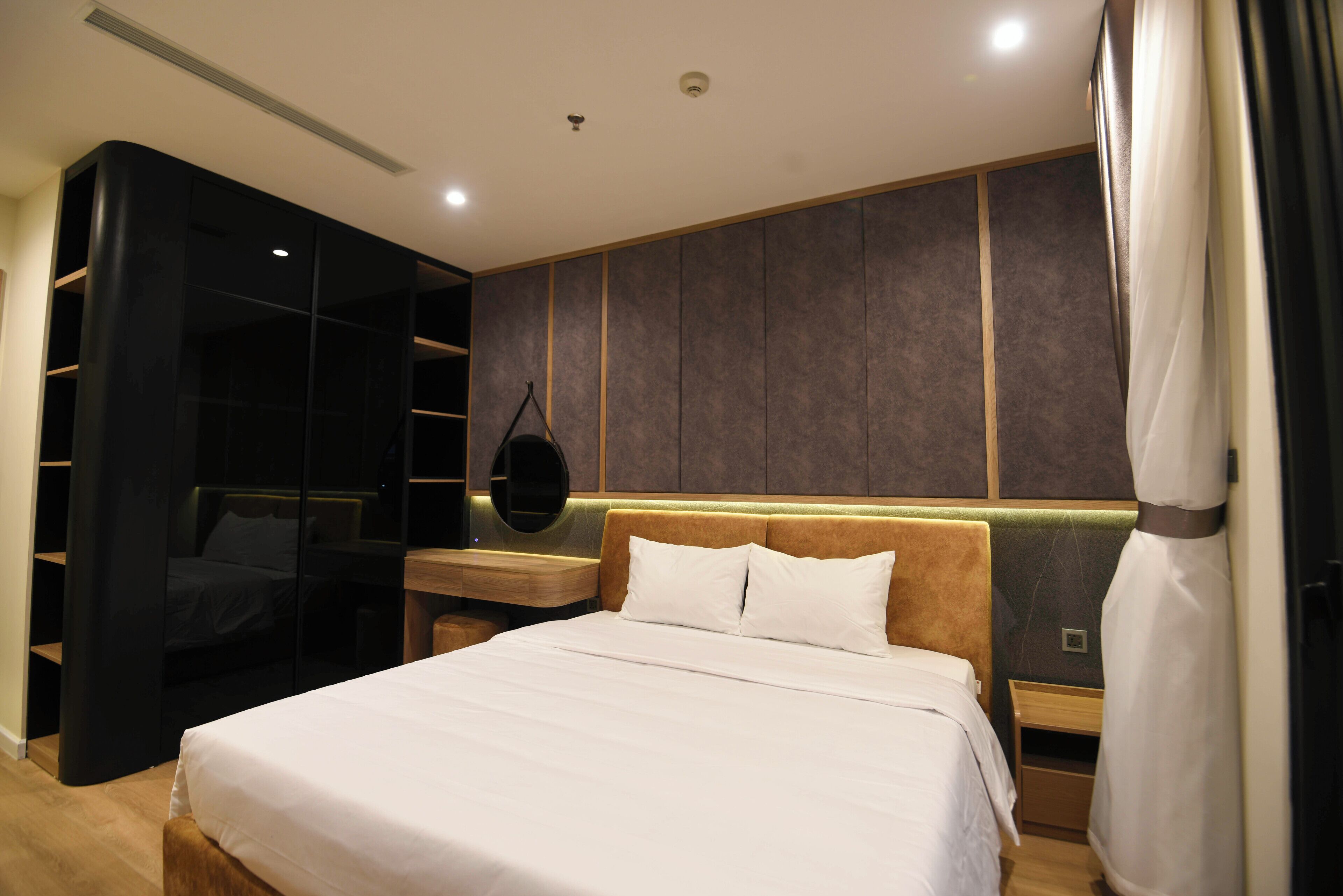 A modern hotel room with a large bed, a built-in wardrobe, and a bedside table.