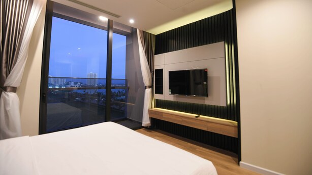 Un hotel moderno con una cama grande, un televisor montado en la pared y vistas de la ciudad a través de amplias ventanas.