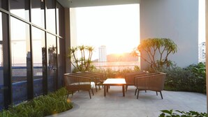 Un área de estar al aire libre con un diseño moderno, con una mesa y sillas, rodeada de vegetación y vistas a un paisaje urbano.