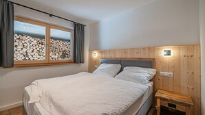 A bedroom with a bed, a window with curtains, a headboard with wall-mounted lights, and a wooden nightstand. - Two Alpine flats with charm (Wald im Pinzgau)