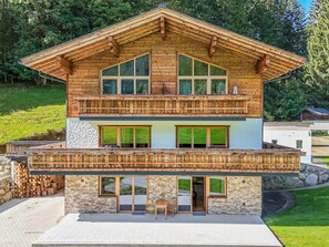 Un chalet de madera de dos pisos, con balcón, fachada de piedra y ventanas grandes.