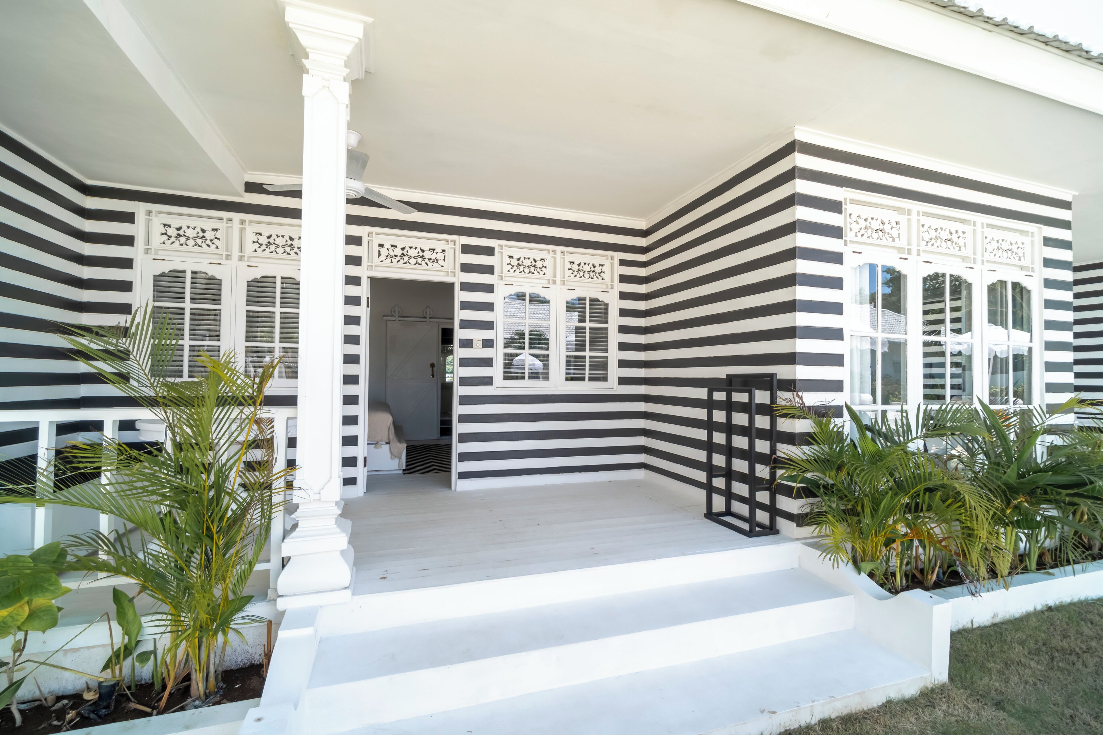 A building with a black and white striped exterior, a white porch with steps, and decorative window grills.