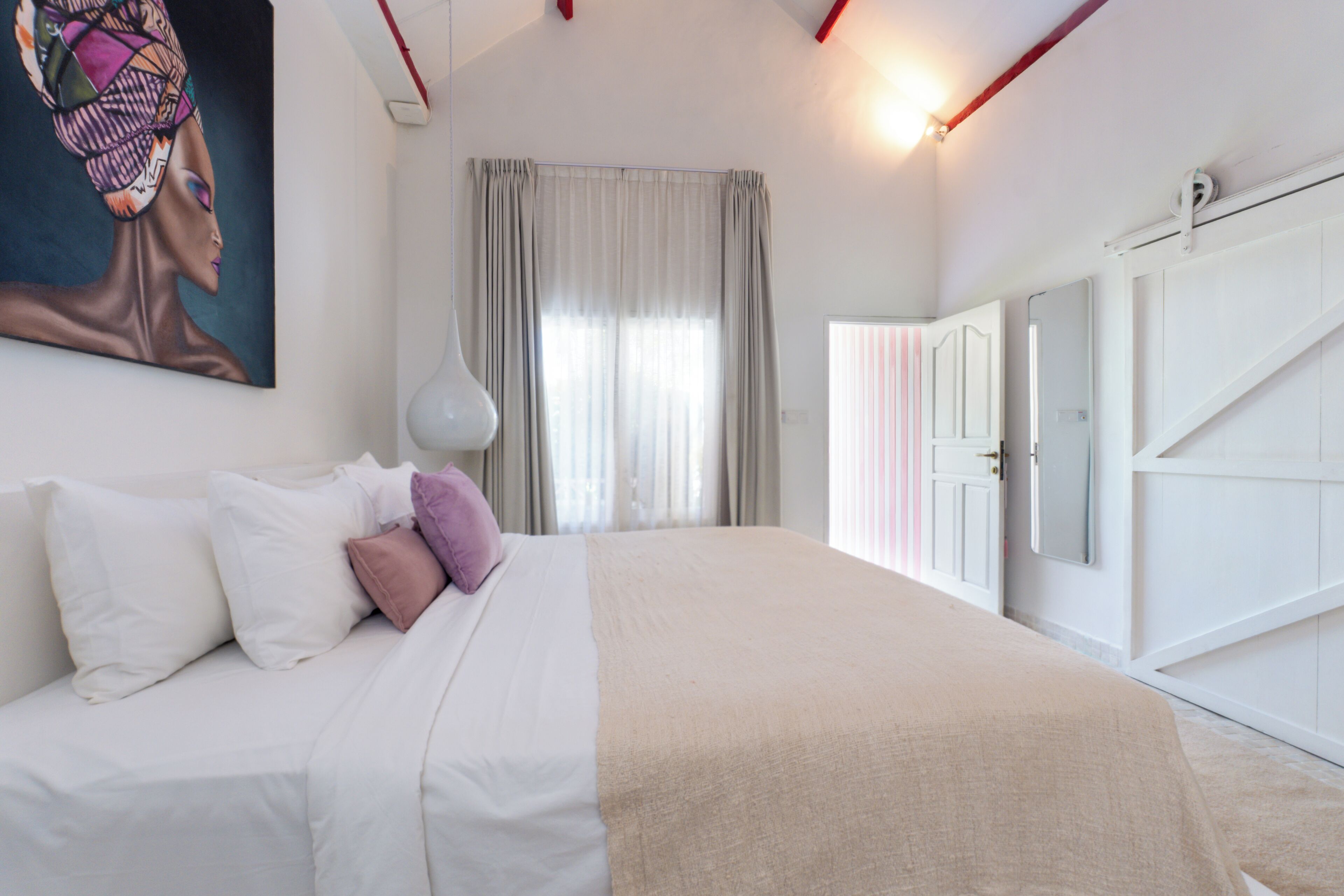 A bedroom with a bed, a painting, a window with curtains, and a wardrobe.