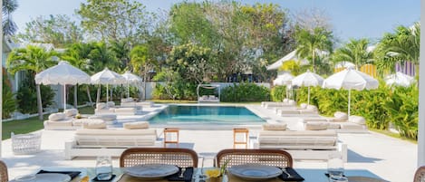 A poolside dining area with white umbrellas, lounge chairs, and a clear view of the pool.