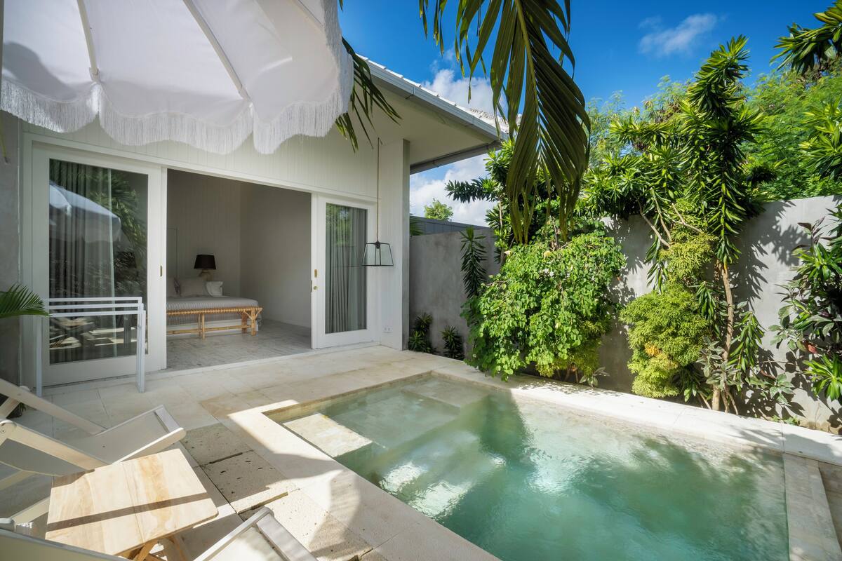 Una casa moderna amb una piscina, un porxo cobert i vegetació exuberante.