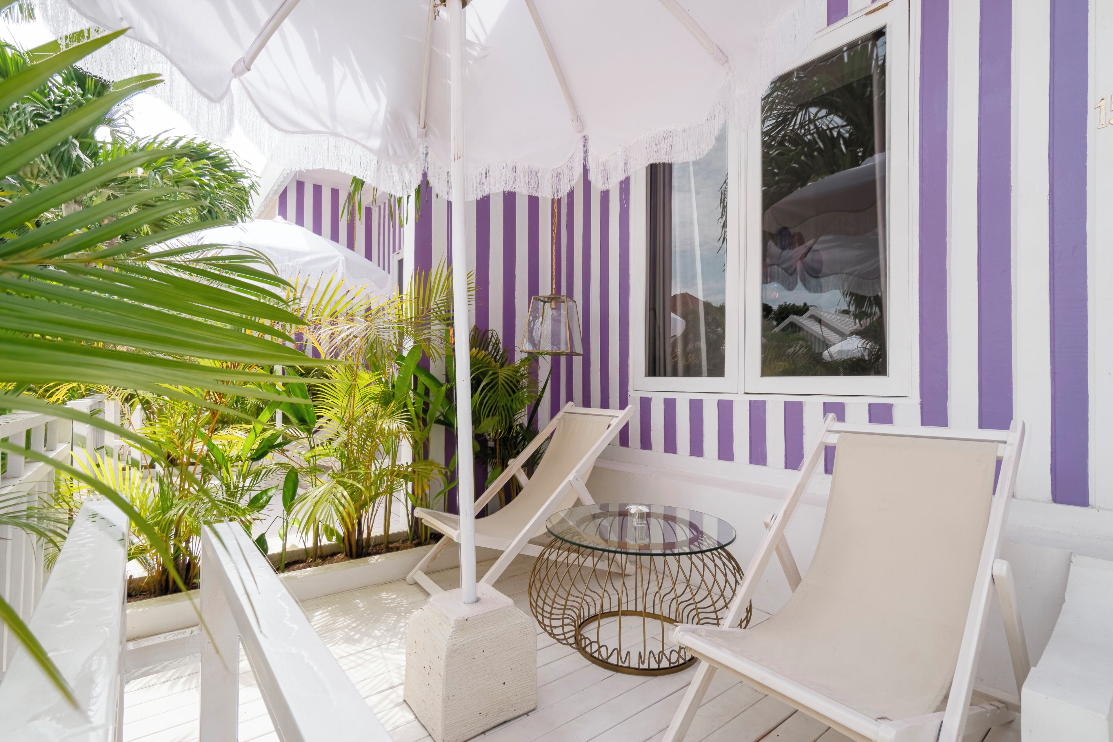 A covered outdoor seating area with white and purple striped walls, a glass table, and lounge chairs.