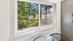 A room with a large window offering a view of a forested area. - Sunny Point 2BR with Deck & Mountain Views (Juneau)