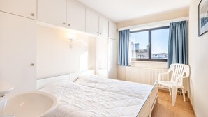 A modern bedroom with a bed, a white sink, a window with curtains, and a view of buildings outside.
