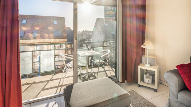 A balcony with a table and chairs, a sofa, a lamp, and a small cabinet. - Cosy family flat centrally located (Koksijde)