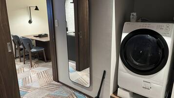 Hotelkamer met een wasmachine, een spiegel, een zithoek met stoelen en een vloer met een patroon.