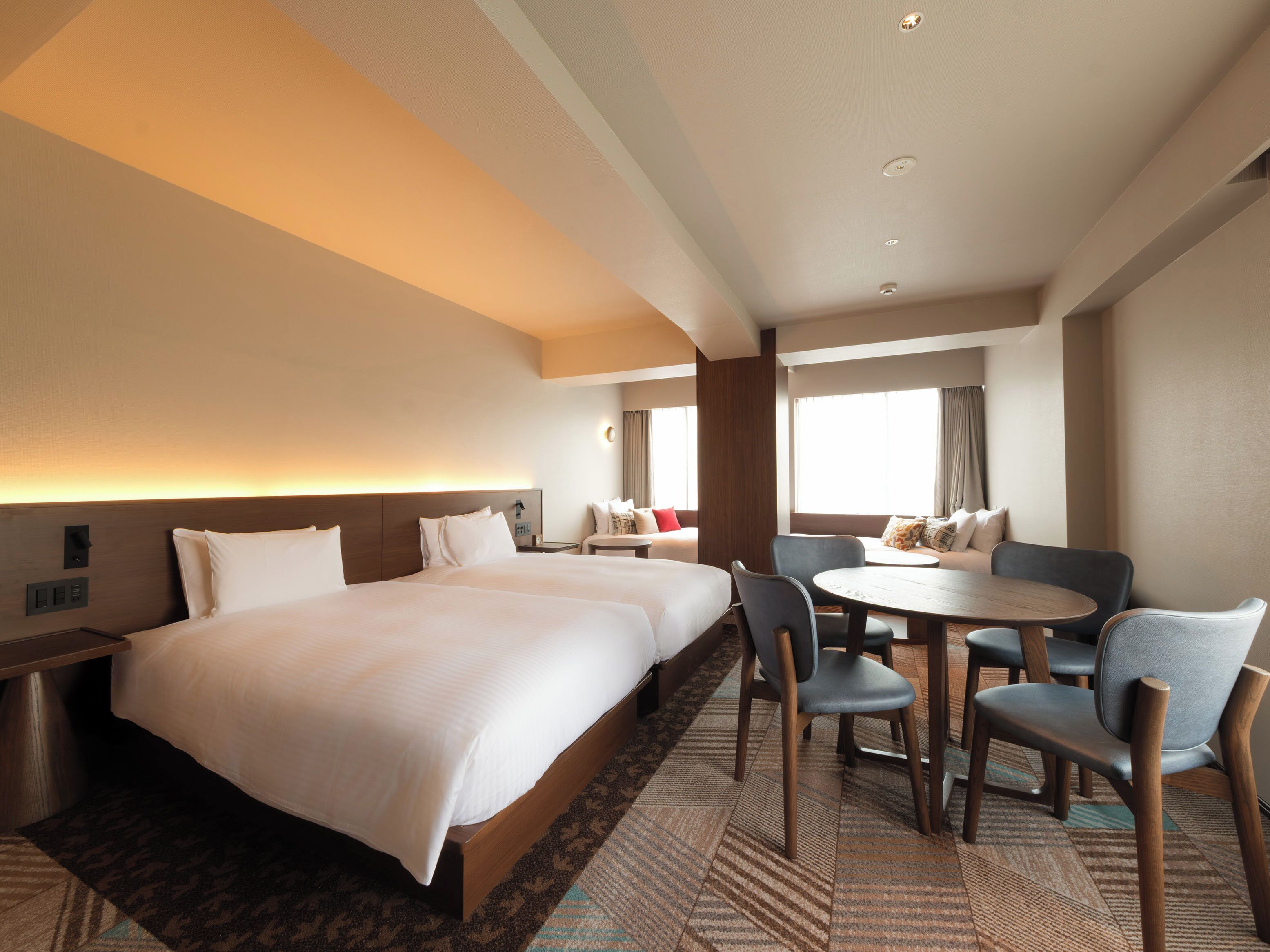Een hotelkamer met twee bedden, een eettafel en een zithoek met stoelen.