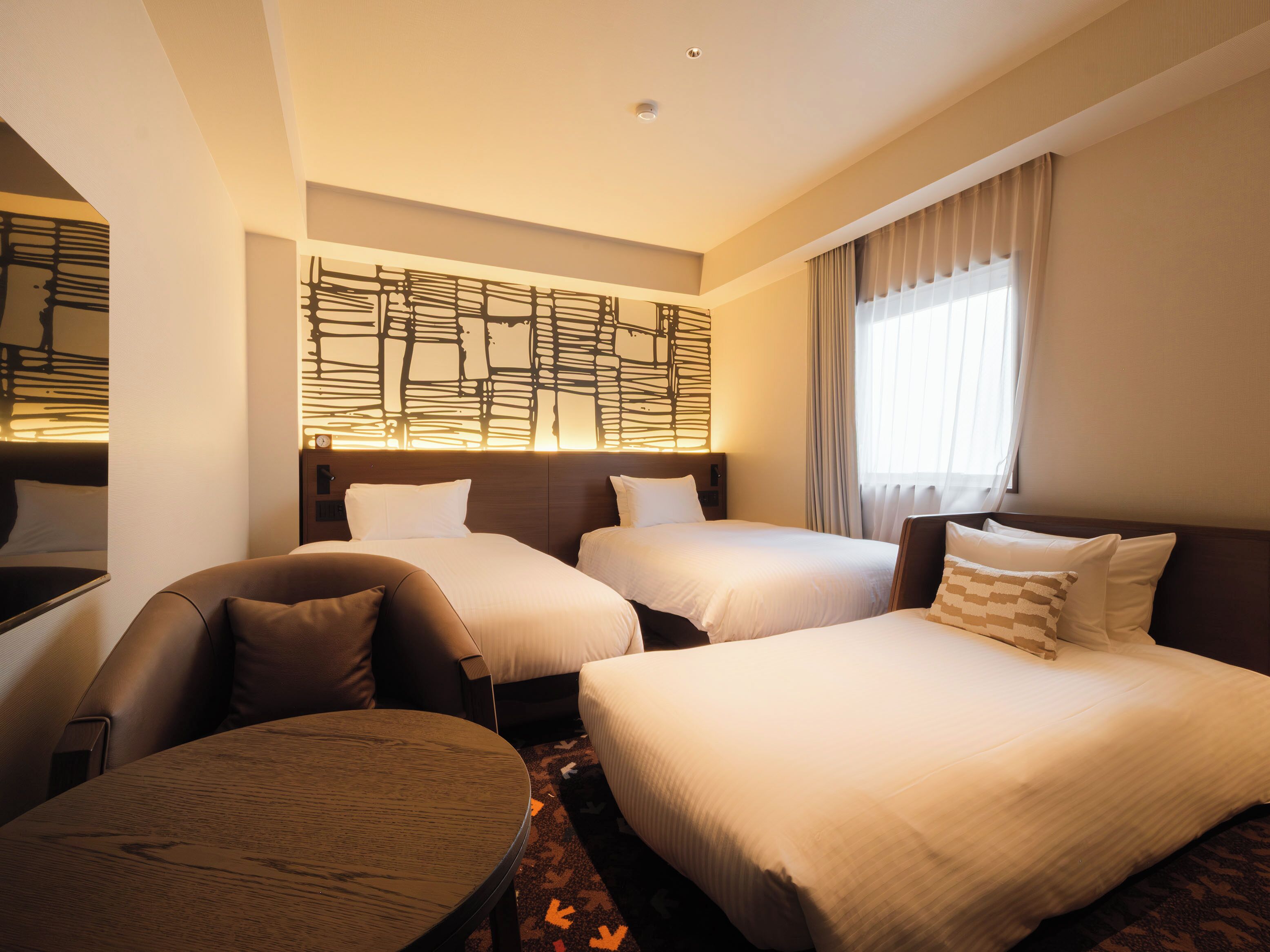A hotel room with two beds, a sofa, a round table, and a decorative wall panel.