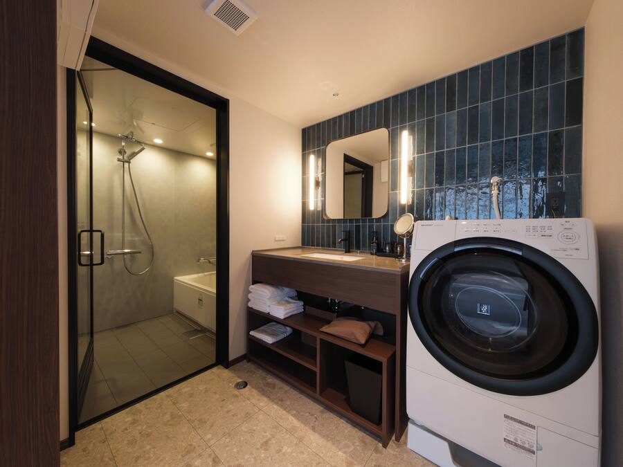 Un bagno moderno con cabina doccia in vetro, lavatrice integrata e mobile lavabo con specchio.