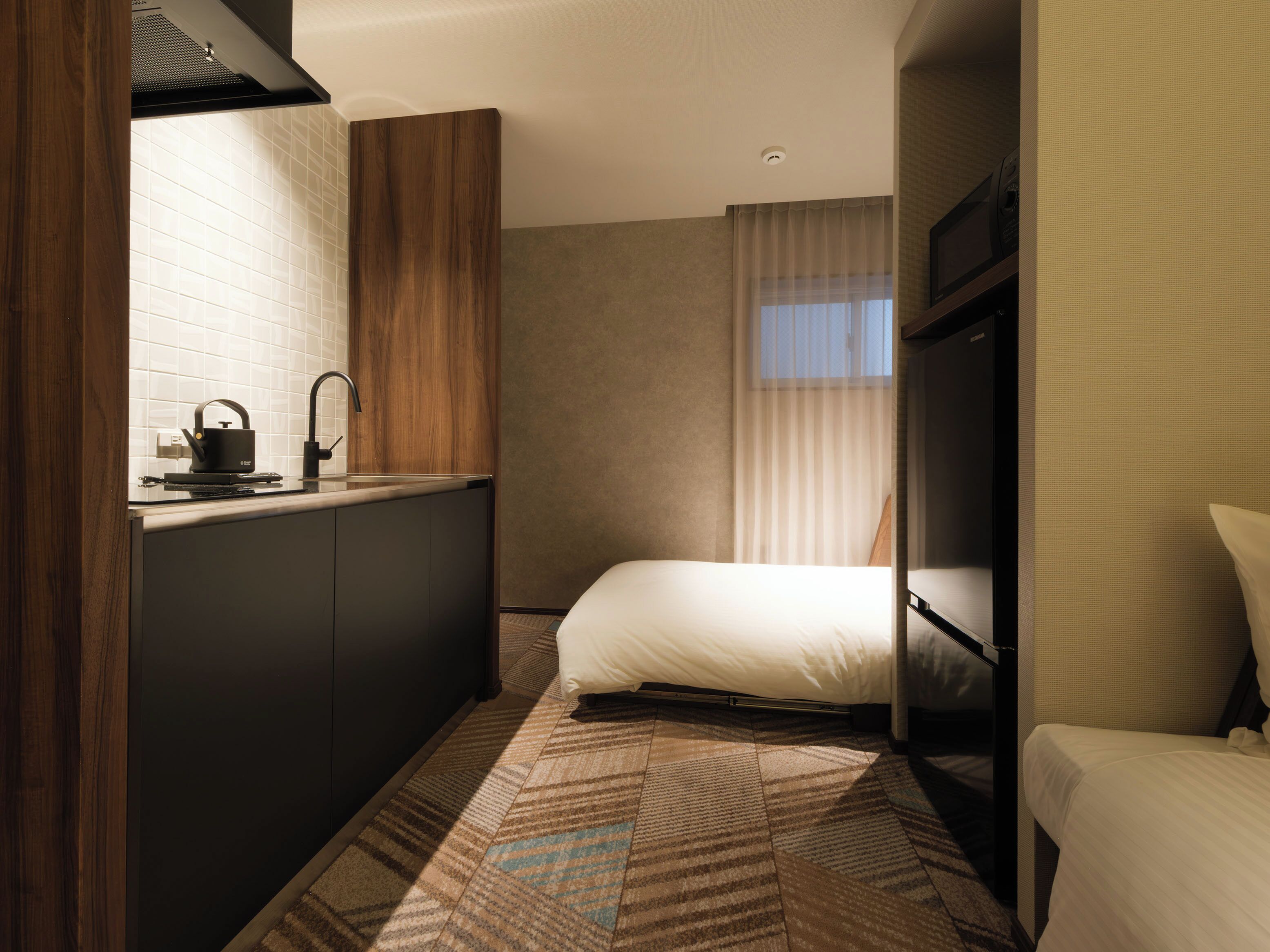 Ein kleines Hotelzimmer mit Küchenzeile, einem Bett und einem Fenster mit Vorhängen.