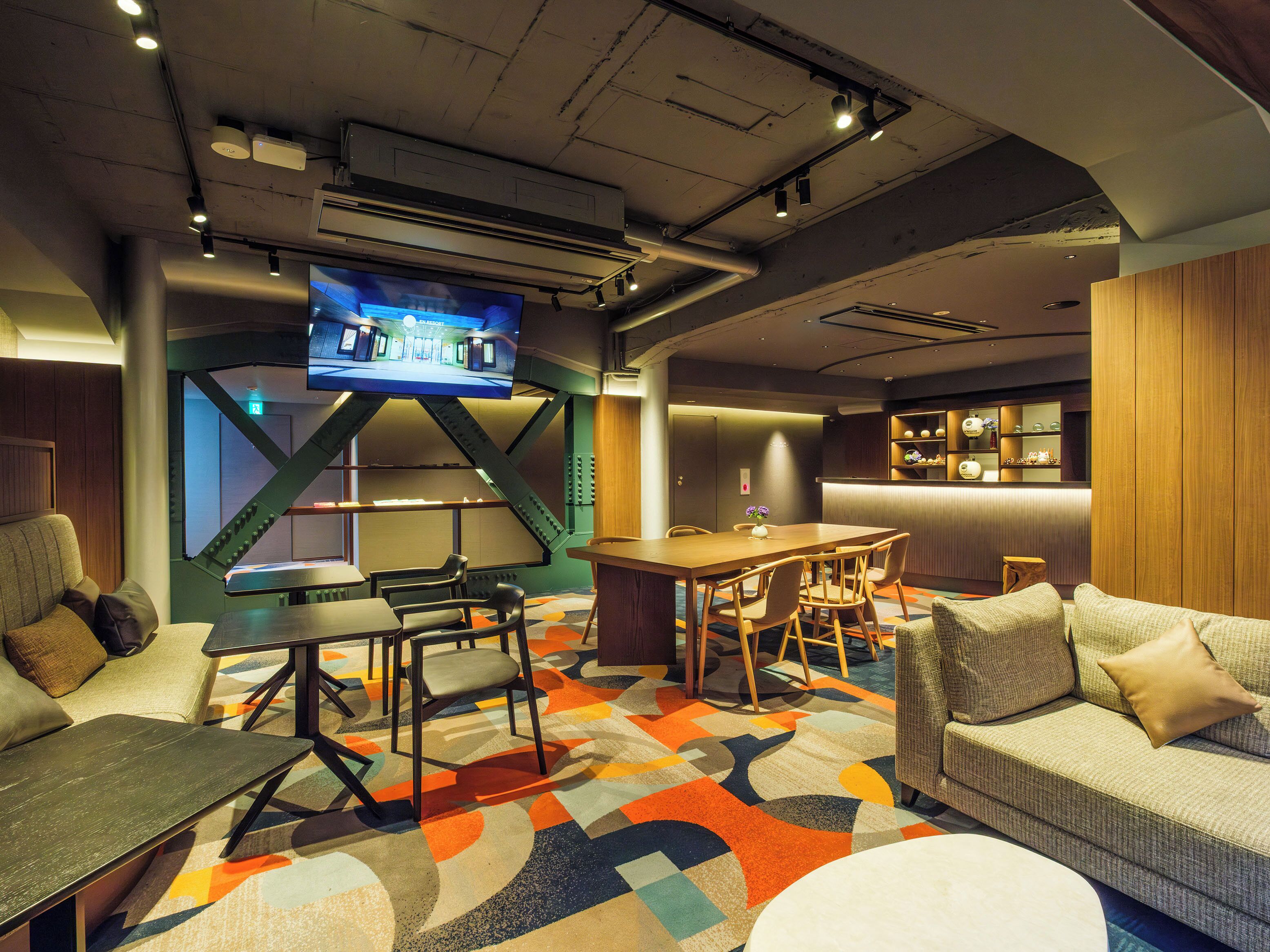 A modern hotel lobby with a large TV, seating area, and a bar.