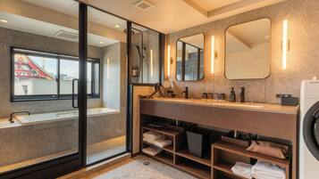 A modern bathroom with a glass shower enclosure, a sink, a vanity with mirrors, and a built-in washing machine.