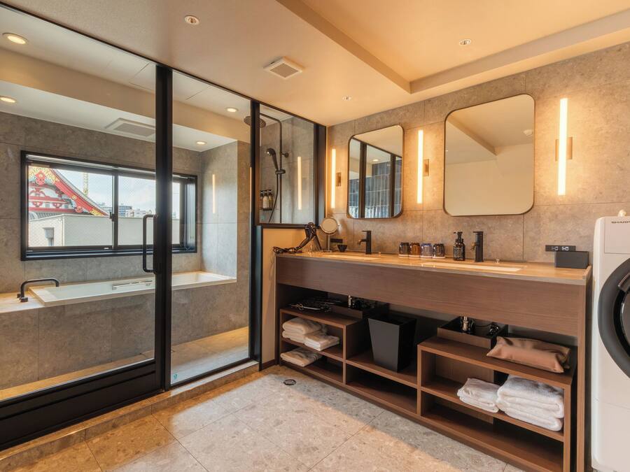 A modern bathroom with a glass shower enclosure, a sink, a vanity with mirrors, and a built-in washing machine.