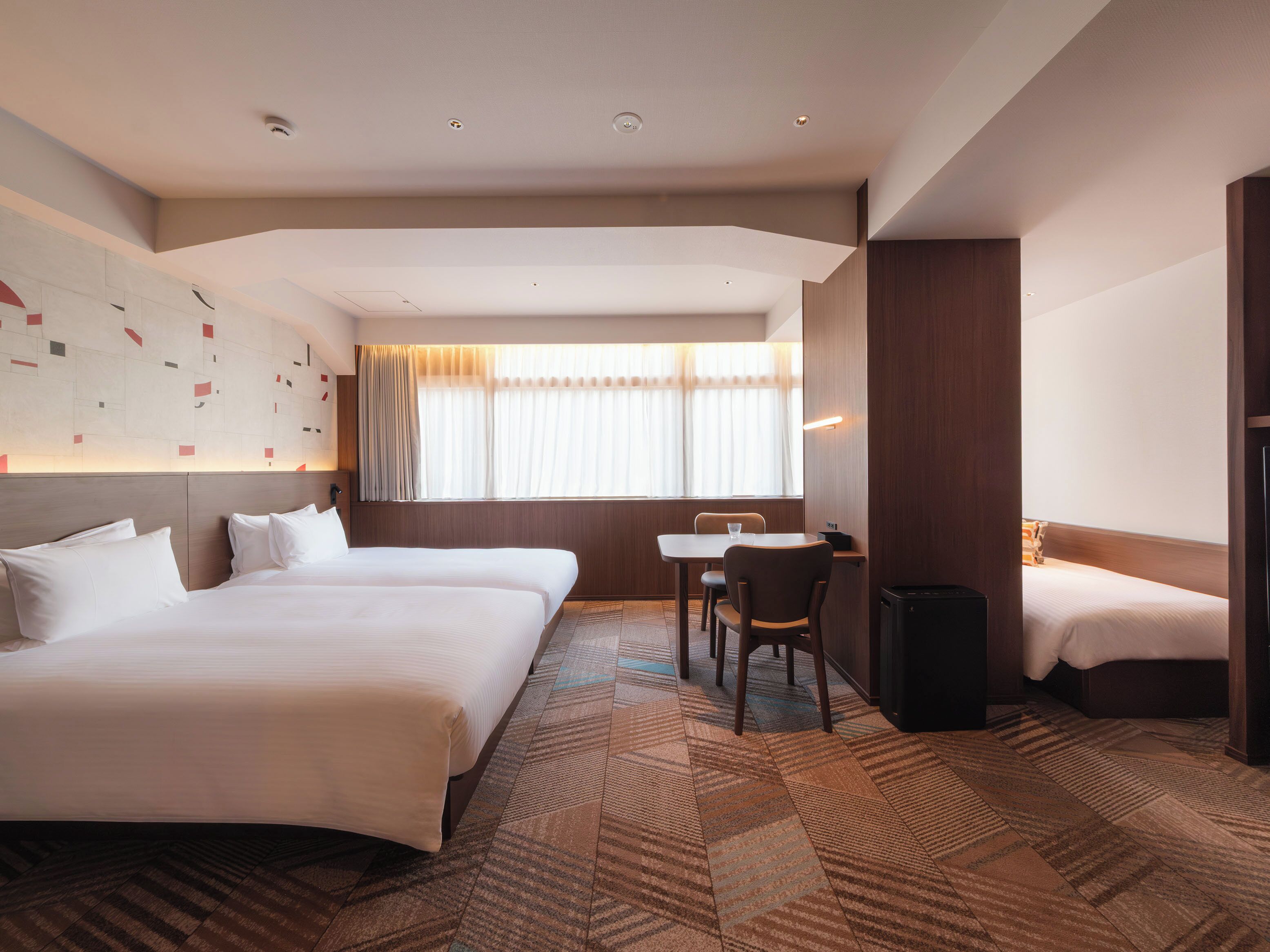 Een hotelkamer met twee bedden, een klein tafeltje en een stoel.