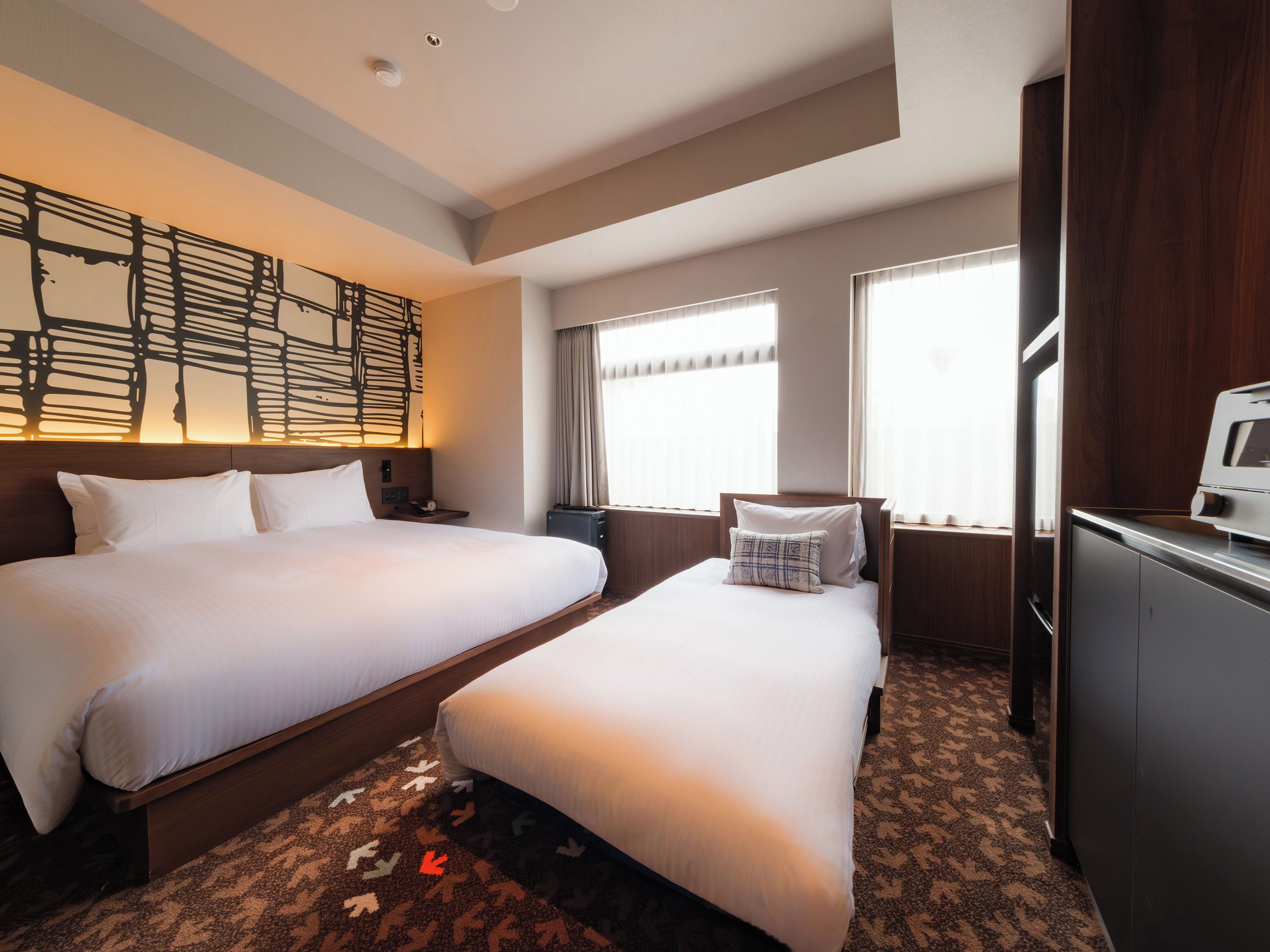 A hotel room with two beds, a desk, a TV, and a large window.