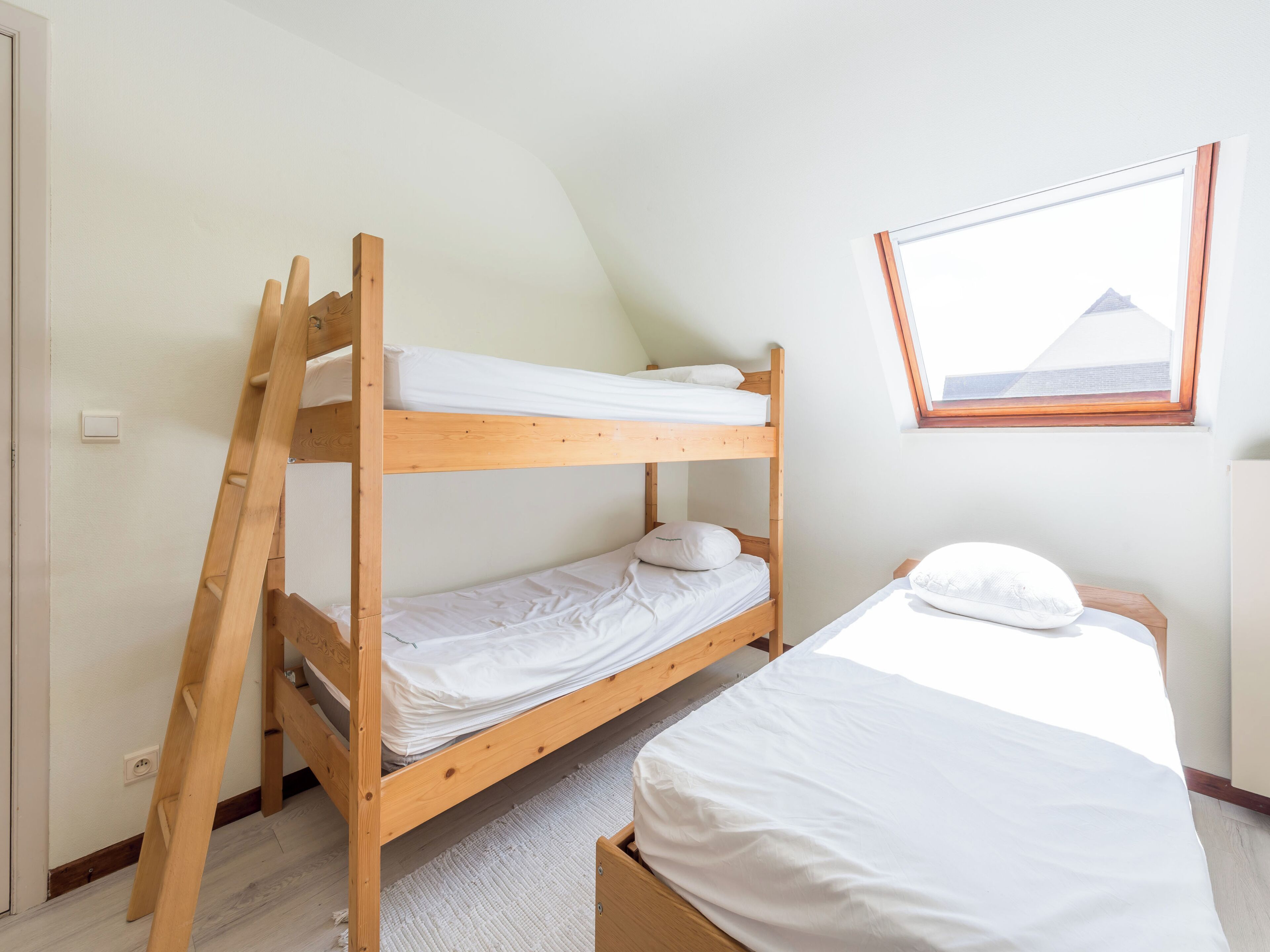 A bunk bed room with a ladder, a window with a view, and a framed picture on the wall.