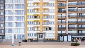 A multi-story residential building with a central entrance, balconies, and a ground-level commercial area with shops. - Spacious family flat with sea view (Koksijde)