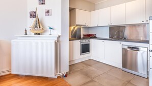 A modern kitchen with white cabinets, stainless steel appliances, and a wooden floor. - Spacious family flat with sea view (Koksijde)