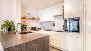 Een moderne keuken met witte kasten, een granieten aanrechtblad, een inbouwoven en een koffiezetapparaat.