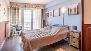 Ein Schlafzimmer mit einem Bett, einem Sessel, einem Nachttisch und einer Wand mit Kunstwerken.