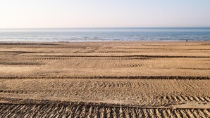 Ein weiter Sandstrand mit Spuren, die zum Wasser führen.