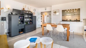 Eine moderne Küche mit Essbereich, mit einem schwarzen Küchenschrank mit Gläsern, einem Holzessttisch mit weißen Stühlen und einem kleinen weißen Tisch mit einem Buch.