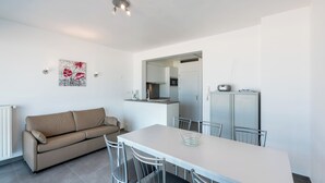 A modern kitchen with white cabinets, a dining table with chairs, and a beige sofa. - Stylish flat with sea view (Koksijde)